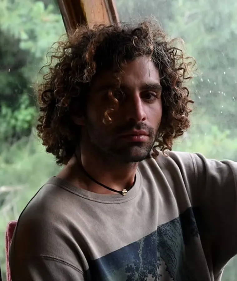 Portrait of Nadi Saddy by a window, green leaves behind him.