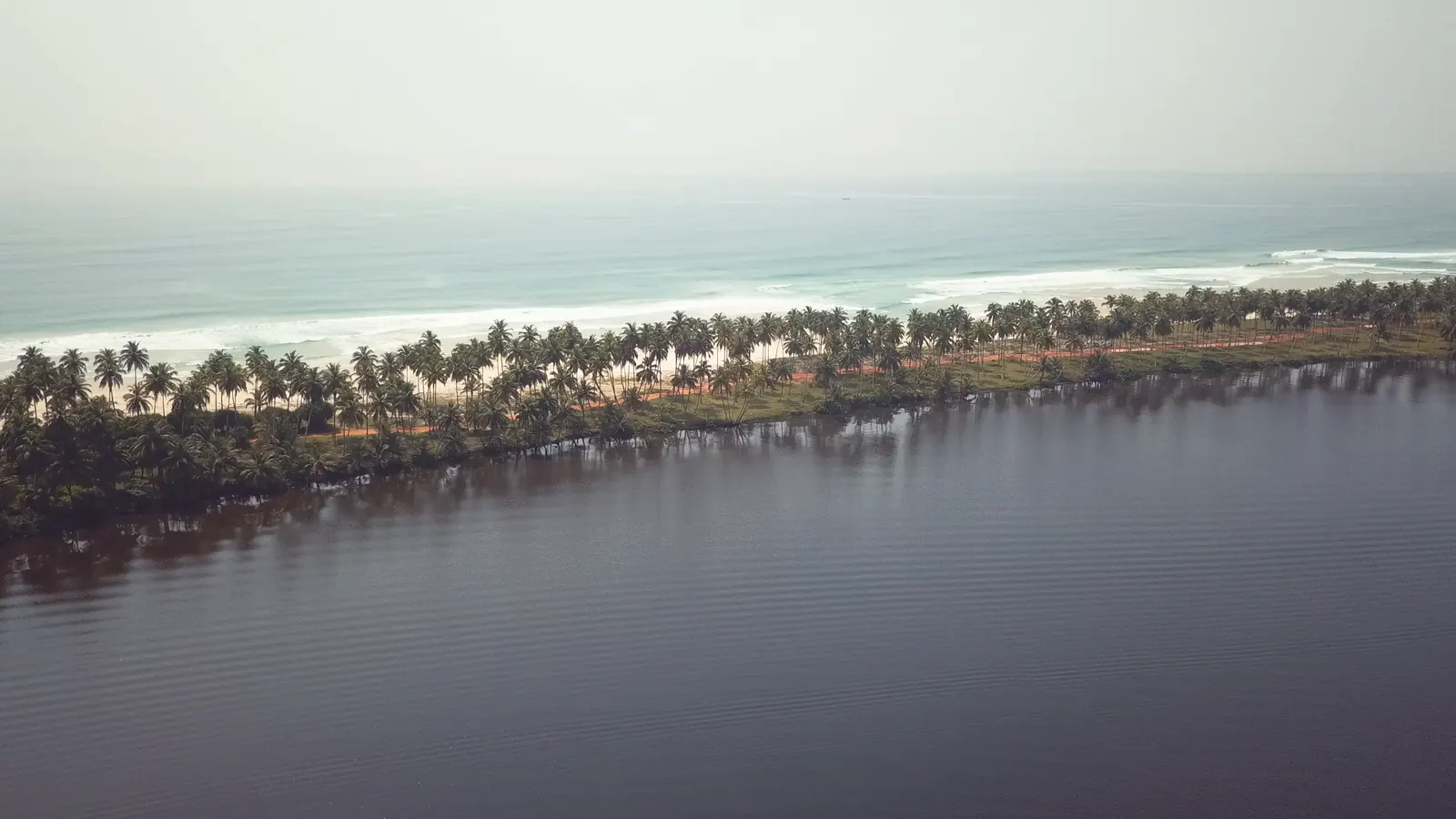 Assinie from the air: the lagoon, a strip of palms, then the Atlantic breaking on the beach.