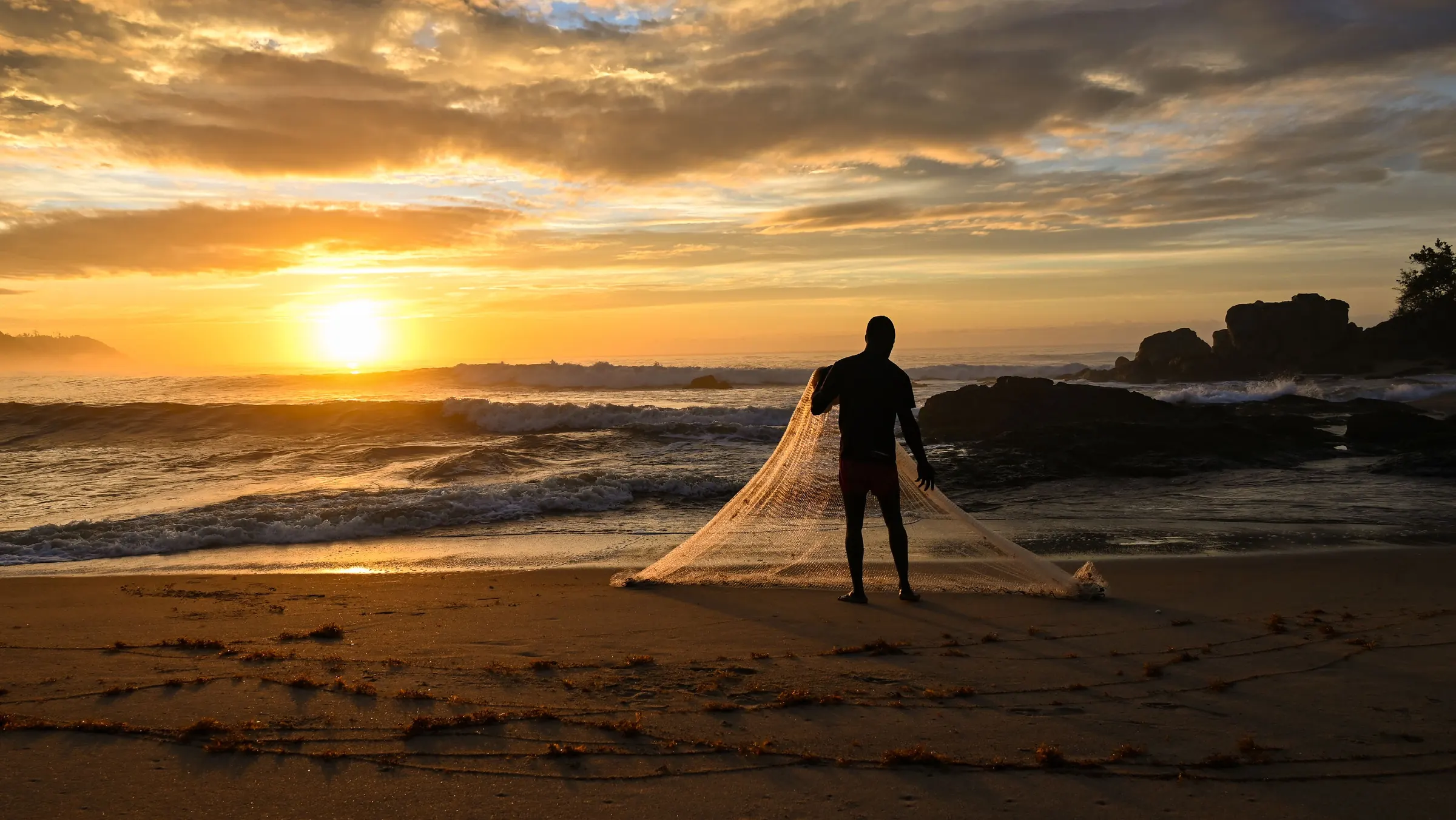 Un pêcheur lance son filet au coucher du soleil sur une plage ivoirienne.