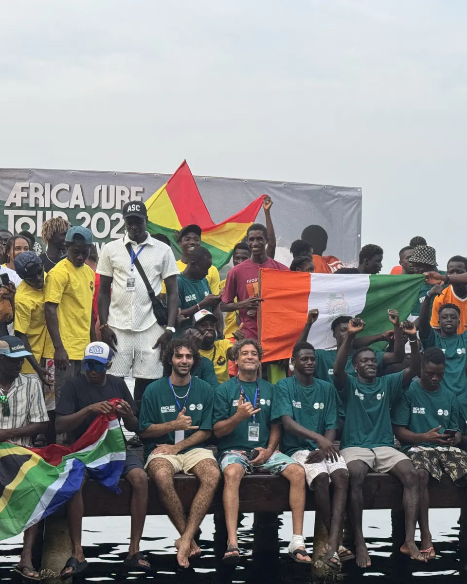Des surfeurs à l’Africa Surf Tour 2025, drapeaux levés devant la banderole de l’événement.