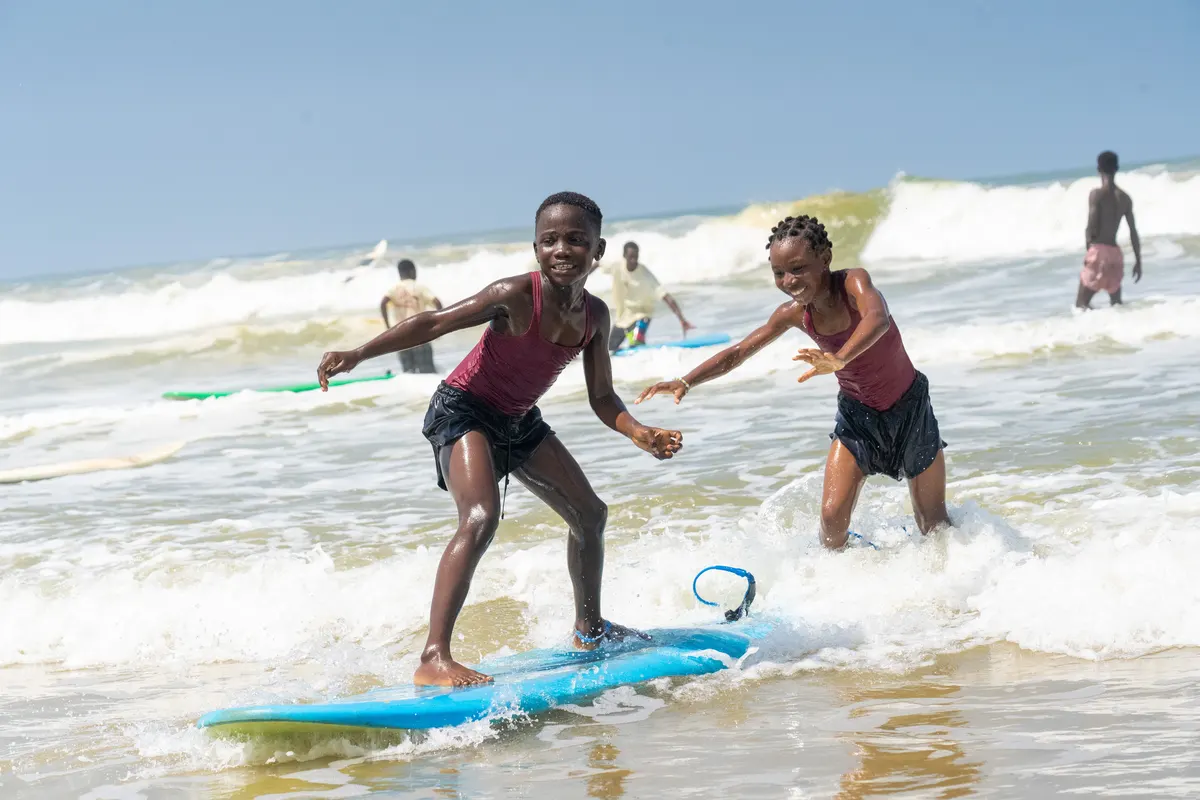 Two young surfers riding a foam board together in the white water.