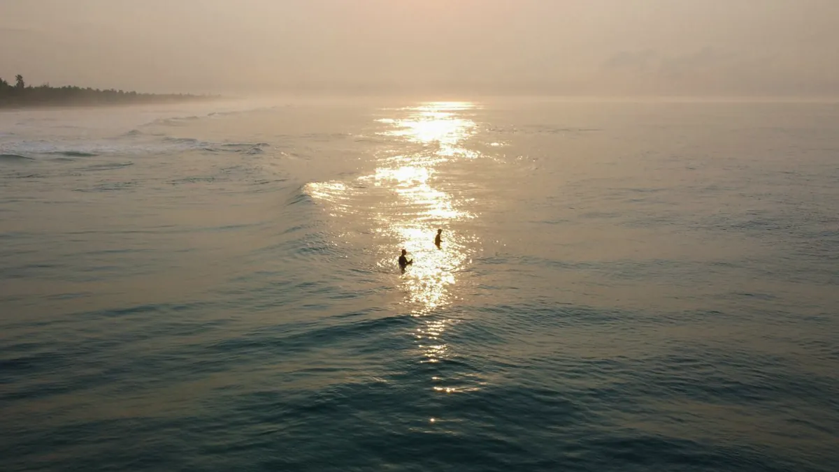 Deux surfeurs qui attendent dans l’eau, dans le reflet du coucher de soleil.