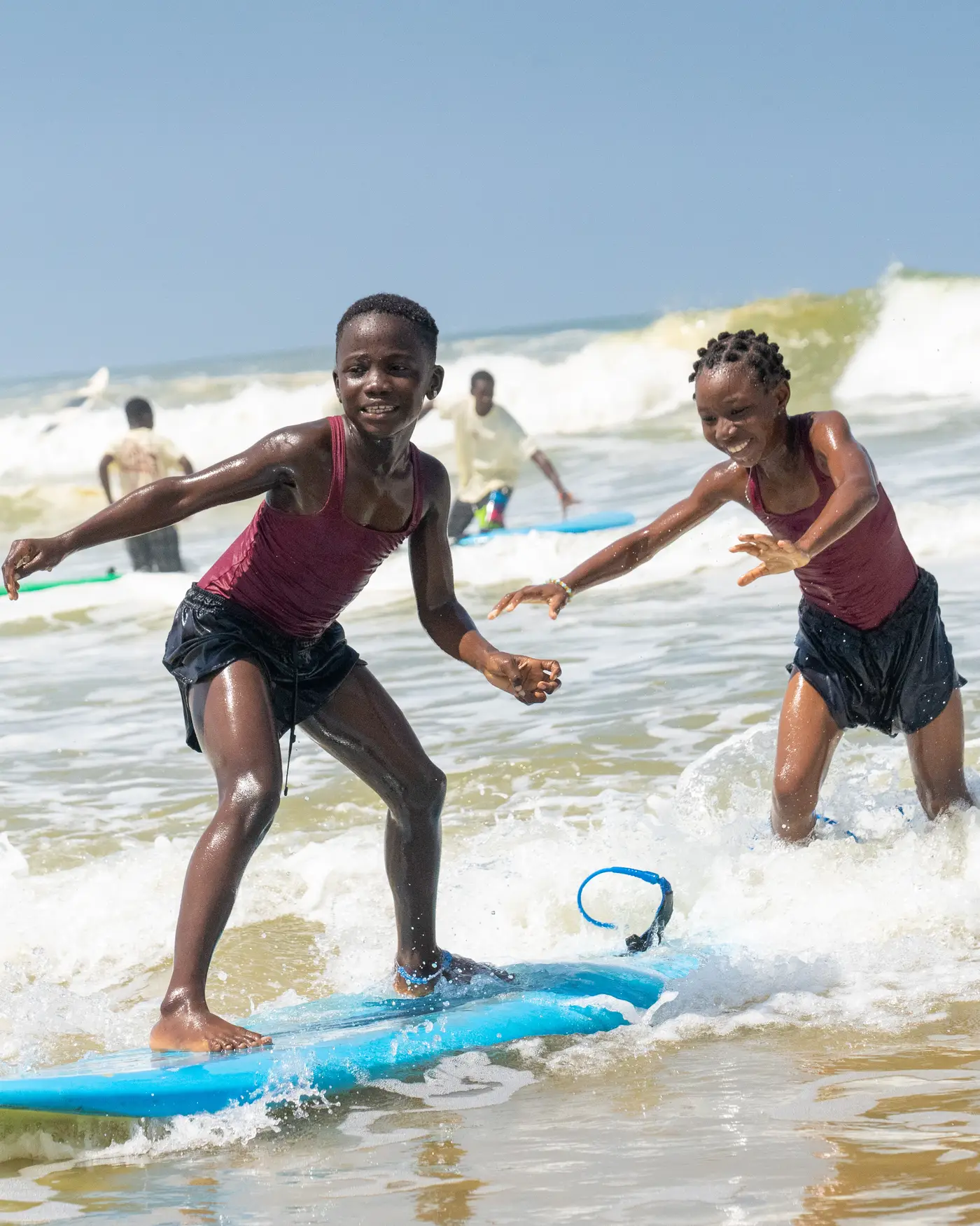 Deux filles éclatent de rire, debout sur une planche de surf dans l’écume.