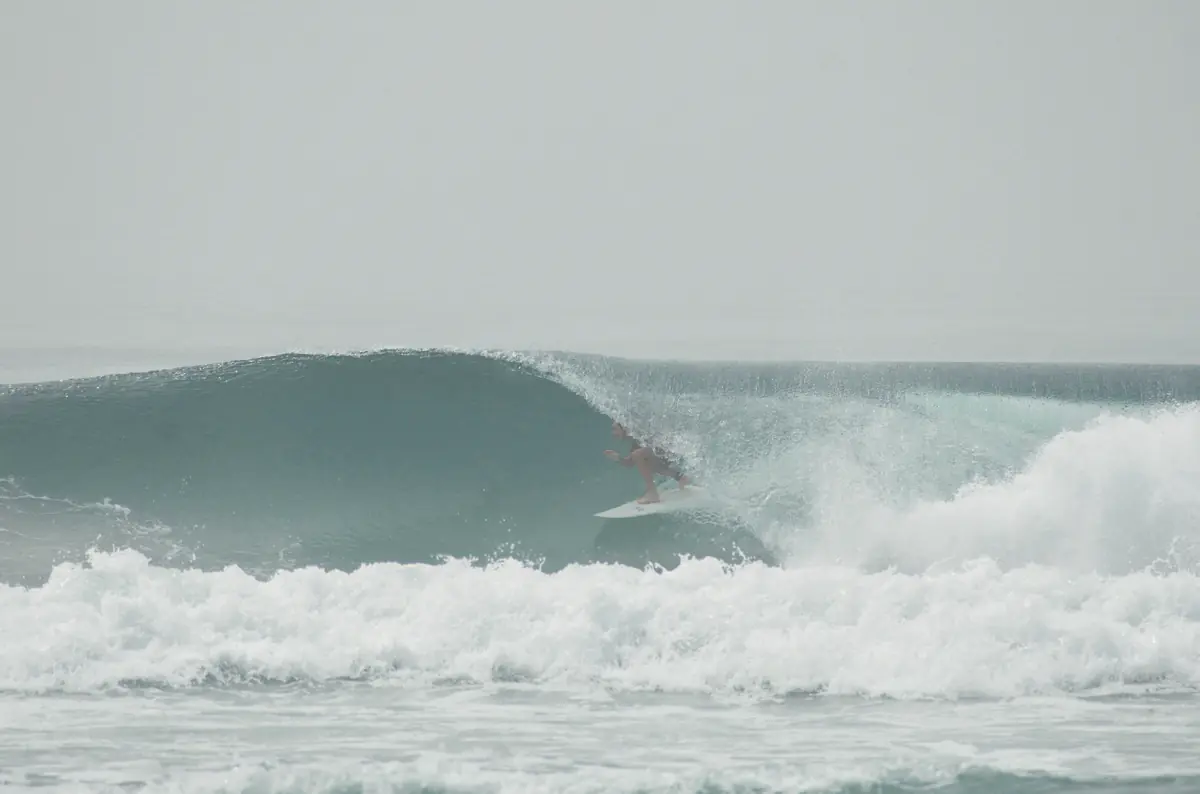 A surfer crouched in the barrel of a wave on a misty day.