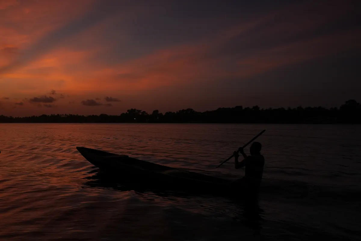 A pirogue on the water under a red dusk sky.