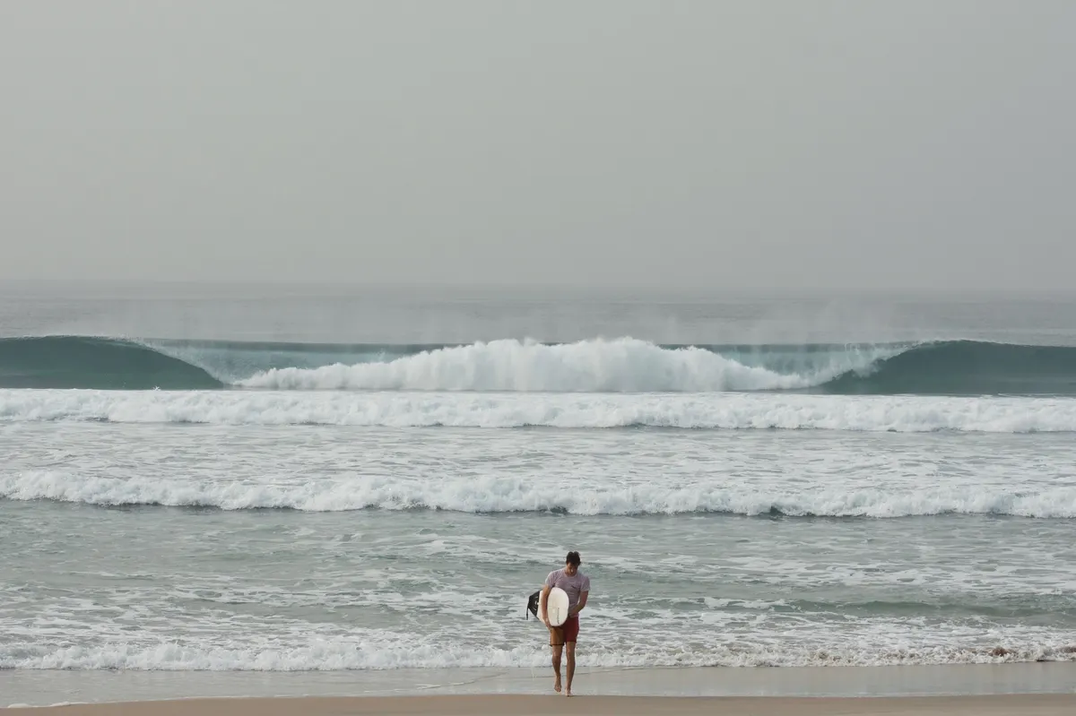 A surfer on the sand, board under his arm, watching the waves.