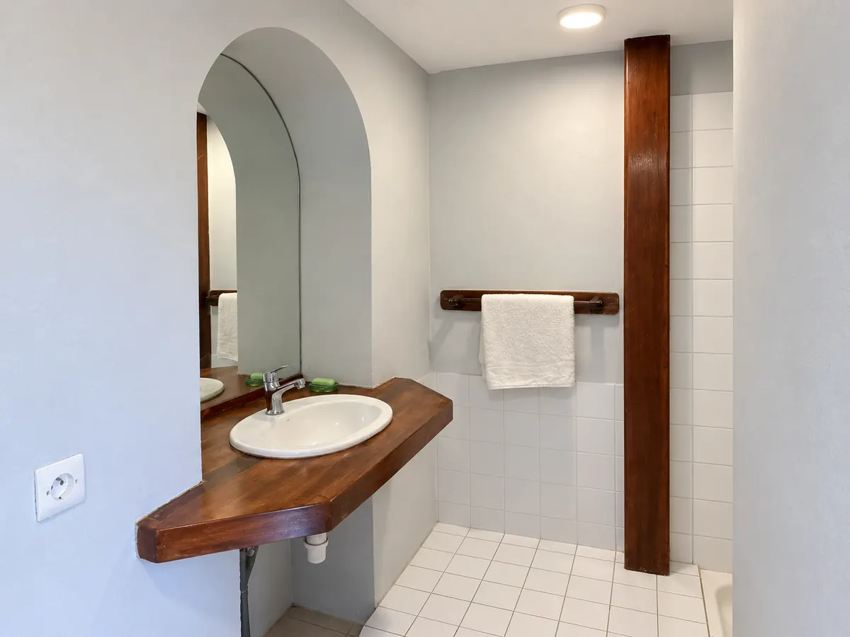 The washbasin on a wooden counter, under an arched mirror.
